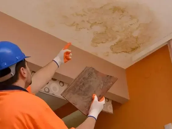 Worker in a hard hat inspecting a water-stained ceiling panel