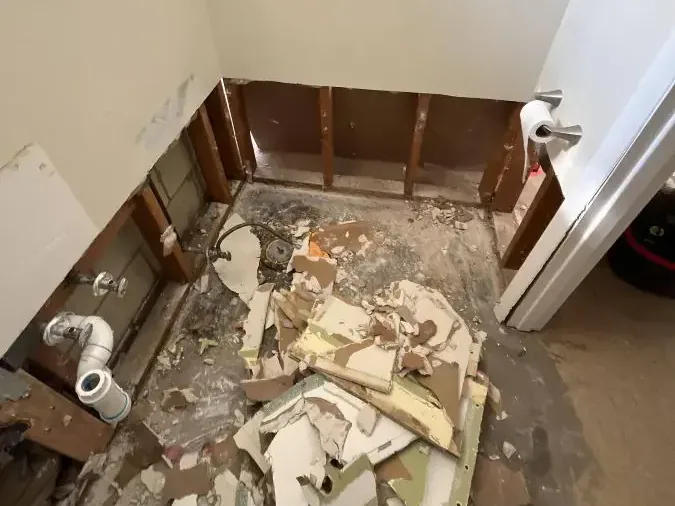 Opened lower bathroom walls with exposed framing and debris across the floor