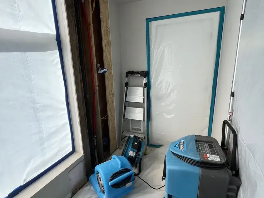 Containment plastic surrounds a blue air mover and dehumidifier inside a room