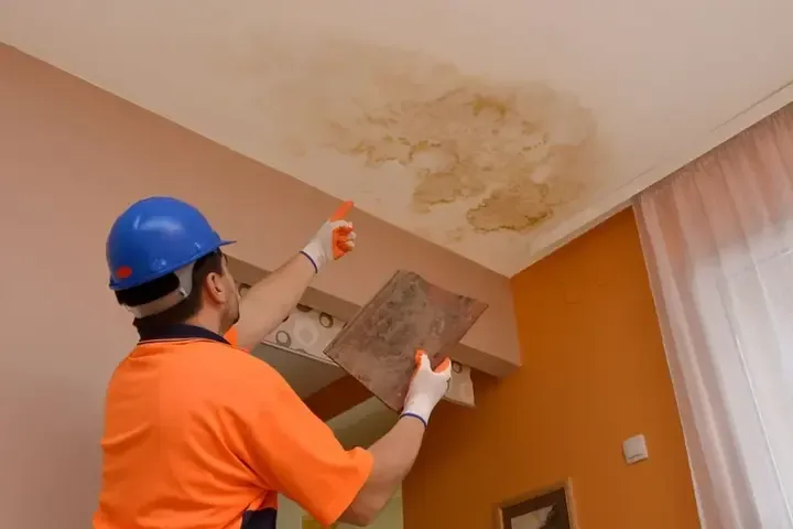 Technician inspecting a water-stained ceiling below a leak
