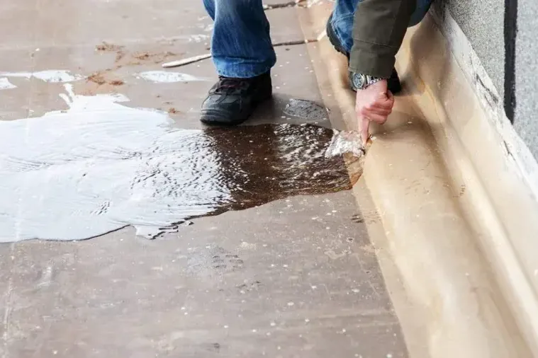 A worker lifts wet floor covering beside water pooled on concrete